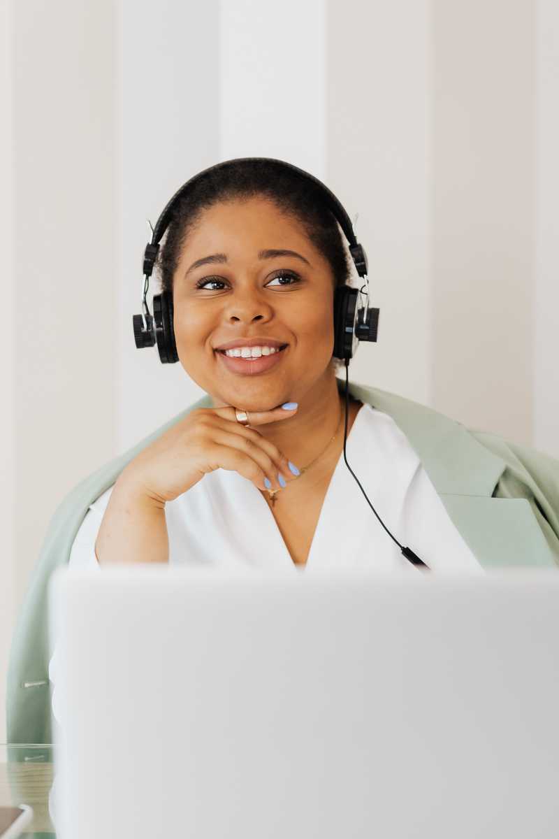Jeune femme derrière son ordinateur, souriant avec un casque audio sur les oreilles. 