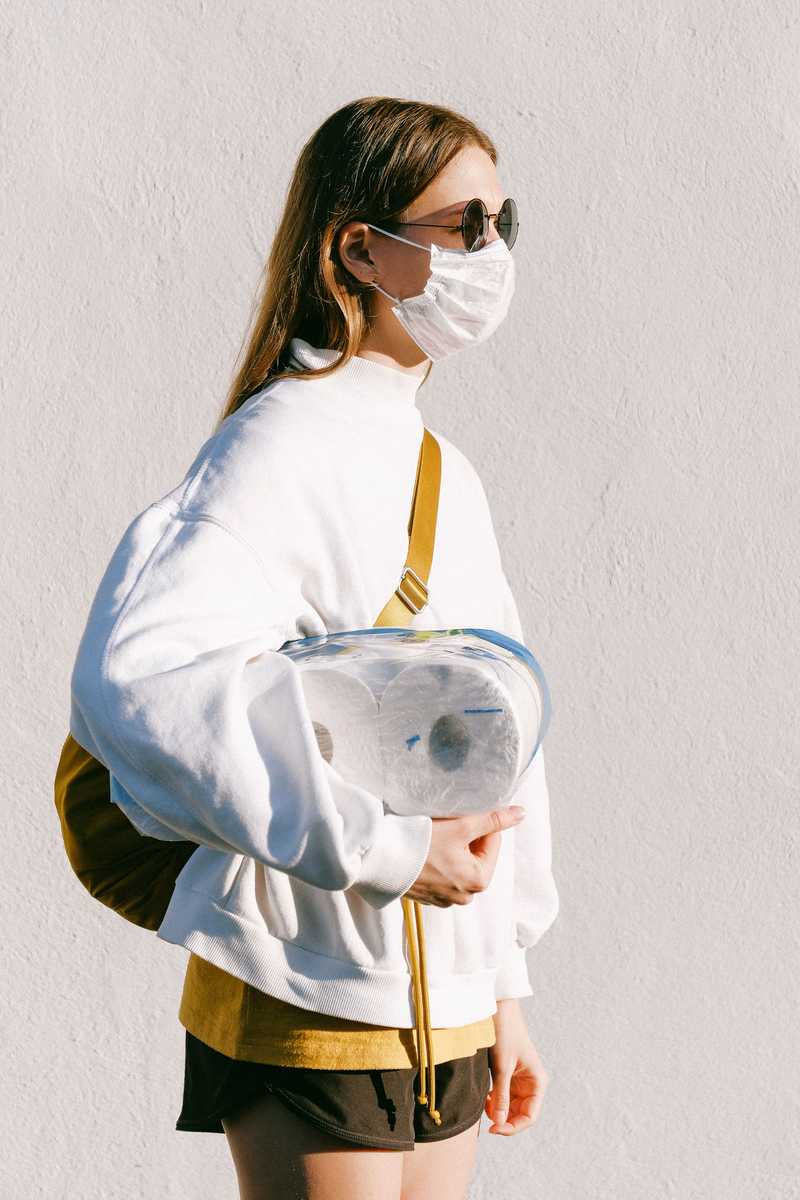 Femme avec un masque, tenant des rouleaux de papier toilette sous le bras